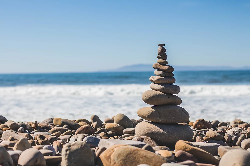 Balanced stone stack by the ocean symbolizing harmony, featured at Elevate Your Organization's Culture and Performance With CEEK.