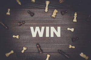 Win text on wooden background with chess pieces, showcasing success only at Elevate Your Organization's Culture and Performance With CEEK.