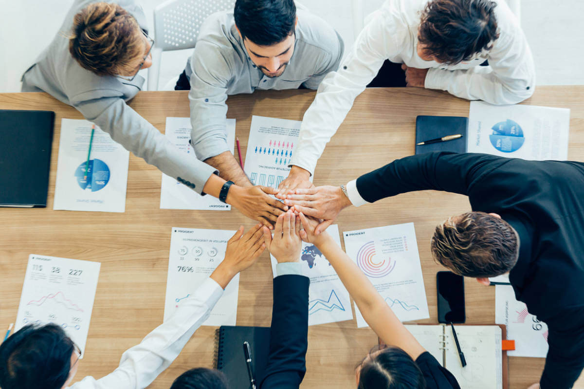Colleagues stacking hands above papers, symbolizing teamwork, only available at Elevate Your Organization's Culture and Performance With CEEK.