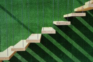 Modern staircase casting shadows on a green wall, symbolizing growth and progress, featured by Elevate Your Organization's Culture and Performance With CEEK.