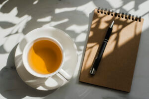 Cup of herbal green tea on marble table with notebook and pen, only available at Elevate Your Organization's Culture and Performance With CEEK.