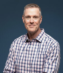 Man in checkered shirt smiling, representing professional growth only available at Elevate Your Organization's Culture and Performance With CEEK.