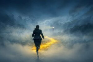 Businesswoman running through fog towards a lighthouse in the distance.